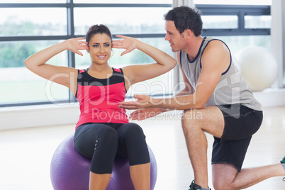 Trainer helping woman do abdominal crunches  on fitness ball