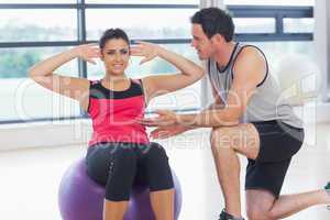 Trainer helping woman do abdominal crunches  on fitness ball