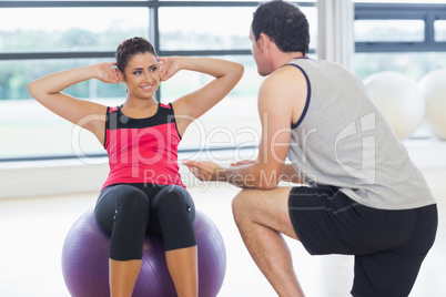 Trainer helping woman do abdominal crunches  on fitness ball