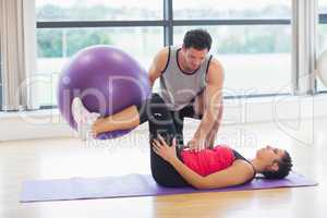 Trainer helping young woman with fitness ball at gym