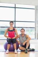 Young woman and man with fitness ball sitting at gym