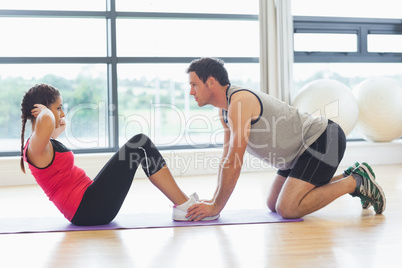 Trainer helping woman do abdominal crunches in gym