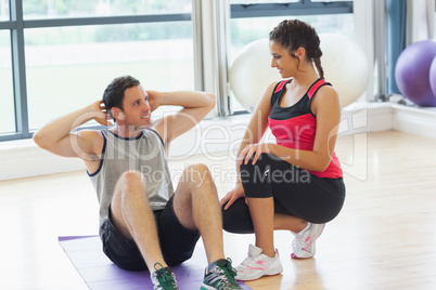 Female trainer looking at man do abdominal crunches