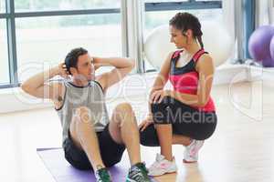 Female trainer looking at man do abdominal crunches