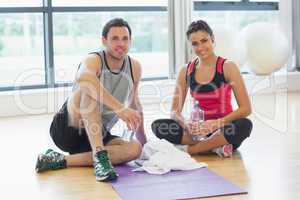 Woman and man with water bottles sitting at gym