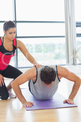 Female trainer assisting man with push ups in gym