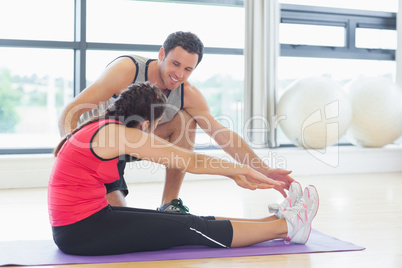 Trainer assisting woman with pilate exercises in fitness studio