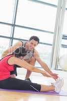 Trainer assisting woman with pilate exercises in fitness studio