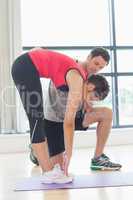 Male trainer assisting woman with stretching exercises in fitnes