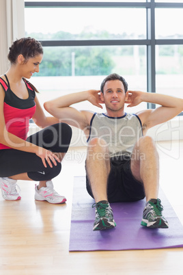 Female trainer watching man do abdominal crunches  on exercise m