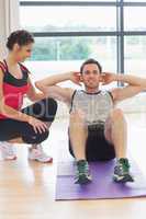 Female trainer watching man do abdominal crunches  on exercise m