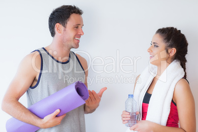 Fit young couple with towel and exercise mat chatting