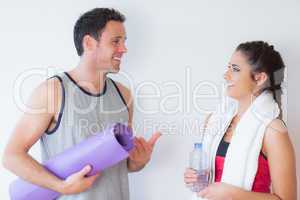 Fit young couple with towel and exercise mat chatting