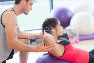 Male trainer helping woman do crunches  on fitness ball at gym