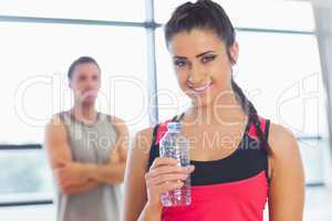 Fit woman holding water bottle with friend in background in exer