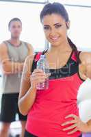 Fit woman holding water bottle with friend in background in exer