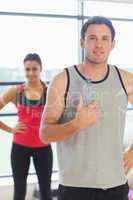 Fit man holding water bottle with friend in background in exerci