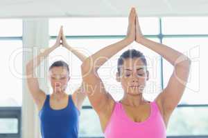 Two women in Namaste position with eyes closed at fitness studio