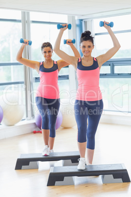 Two women performing step aerobics exercise with dumbbells