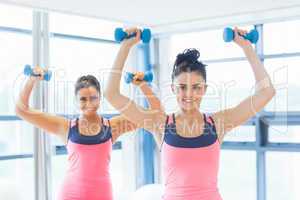 Two fit women lifting dumbbell weights in gym