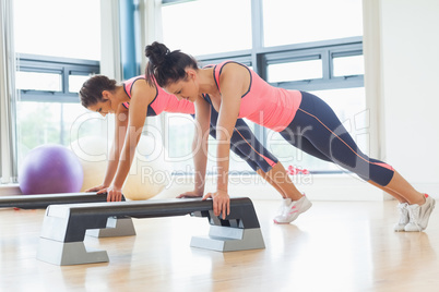 Two fit women performing step aerobics exercise in gym