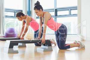 Fit women performing step aerobics exercise in gym