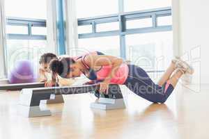 Two women performing step aerobics exercise in gym