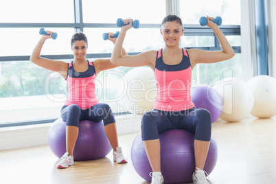 Two fit women exercising with dumbbells on fitness balls