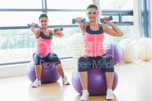 Two fit women exercising with dumbbells on fitness balls