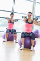 Two fit women exercising with dumbbells on fitness balls
