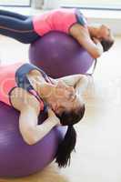 Two fit young women stretching on fitness balls in gym