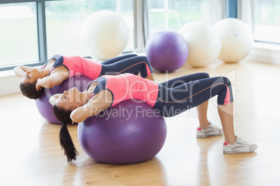 Two fit women stretching on fitness balls in gym