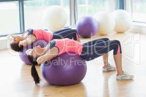 Two fit women stretching on fitness balls in gym