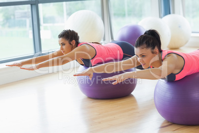 Two fit women stretching out hands on fitness balls in gym