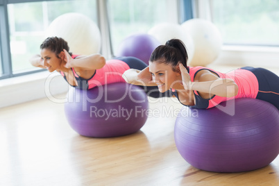 Two fit women exercising on fitness balls in gym