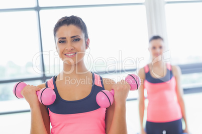 Fit woman lifting dumbbell weights with friend in background at