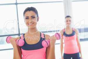 Fit woman lifting dumbbell weights with friend in background at