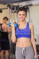 Sporty woman with dumbbell amd man using lat machine in the gym