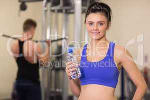 Woman with water bottle while man using lat machine in gym