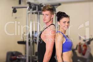 Sporty woman and man standing back to back in the gym