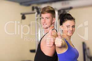 Sporty couple gesturing thumbs up in the gym