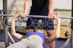 Trainer helping woman to lift the barbell bench press in gym