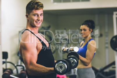 Young man and woman using dumbbells in gym