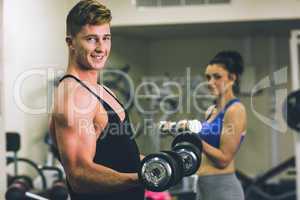 Young man and woman using dumbbells in gym