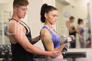 Male trainer helping woman with the dumbbells in gym