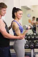 Male trainer helping young woman with the dumbbells in gym
