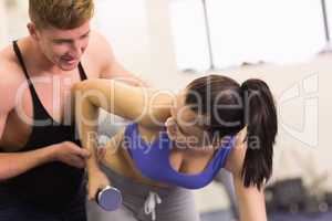 Male trainer helping woman with dumbbell in the gym