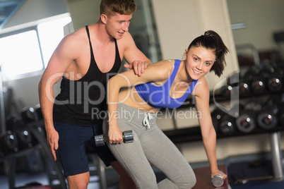 Trainer helping young woman with dumbbells in the gym