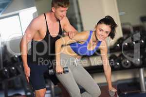 Trainer helping young woman with dumbbells in the gym