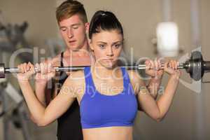 Trainer helping fit woman to lift the barbell in gym